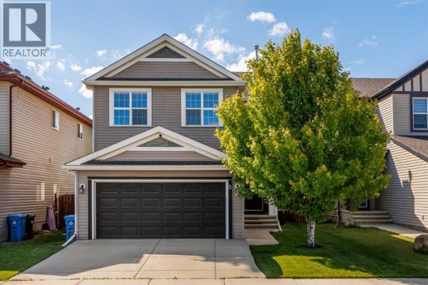 Side exterior view of the house, showing the driveway, lawn, and mature tree. - 5 Copperpond Link Se, Calgary
