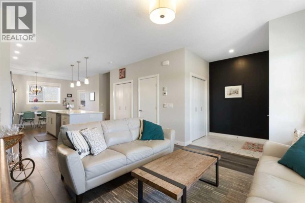 Living room with a sectional sofa, coffee table, and open-concept view to the kitchen. - 5 D'arcy Boulevard, Okotoks