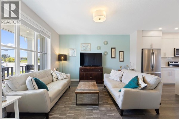 Living room with two sofas, coffee table, television, and view of the adjacent kitchen. - 5 D'arcy Boulevard, Okotoks