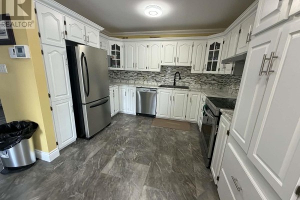 White kitchen cabinets with stainless steel appliances, granite countertops, and a mosaic tile backsplash. - 5 Davis Crescent, Happy Valley Goose Bay