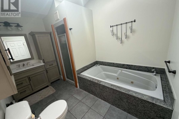 Bathroom with a corner jacuzzi tub, grey tiled surround, vanity, toilet, and glass shower stall. - 5 Davis Crescent, Happy Valley Goose Bay