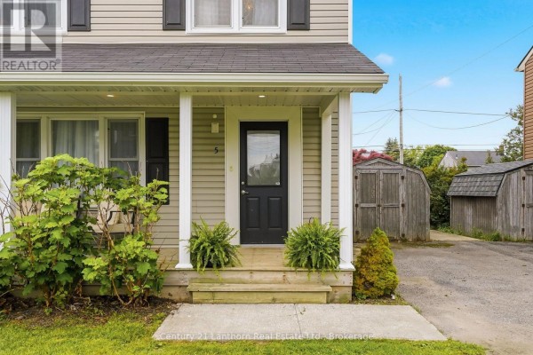 Close-up of the front door and covered porch with potted plants and seating. - 5 Diverbelt Drive, Prince Edward County