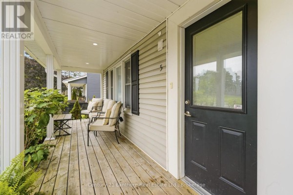 View from the covered porch showing outdoor seating and the front door. - 5 Diverbelt Drive, Prince Edward County