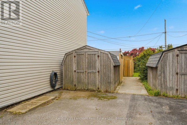 Two wooden sheds are situated on a gravel driveway beside the house. - 5 Diverbelt Drive, Prince Edward County