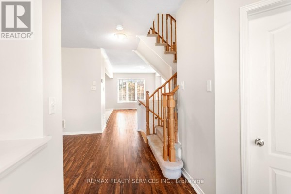 View of a townhouse interior hallway with wood floors, carpeted stairs, and doorways. - 5 Dollery Gate, Ajax