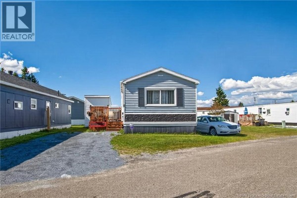 Rear view of the gray mobile home with a green lawn, gravel driveway, and a dark gray storage shed. - 5 Dove Street, Saint John