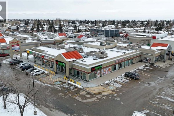 Aerial view of a commercial strip mall with parking lot and surrounding residential homes. - 5 Falsbridge Drive Ne, Calgary