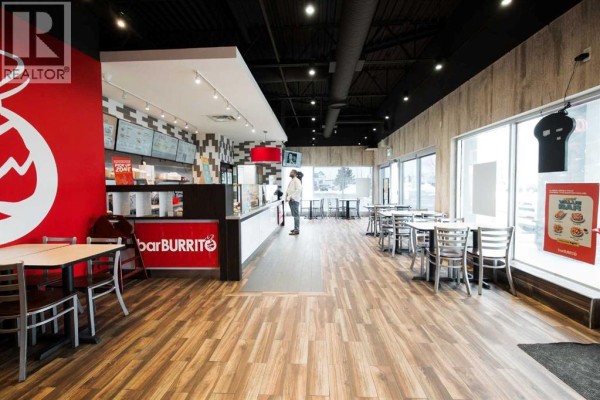 Restaurant interior showing a service counter, dining tables, and large windows overlooking the street. - 5 Falsbridge Drive Ne, Calgary