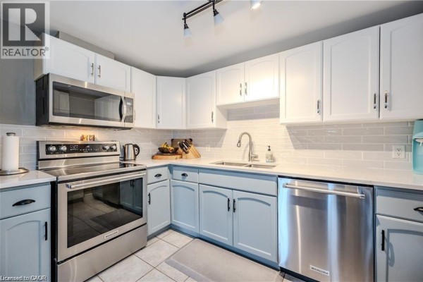 Corner kitchen with white and light blue cabinets, stainless steel appliances, and subway tile backsplash. - 5 Father David Bauer Drive Unit# 301, Waterloo