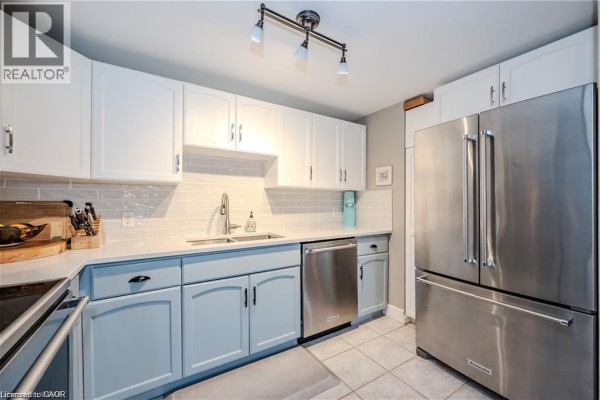 Kitchen view with stainless steel refrigerator, white and blue cabinets, and subway tile backsplash. - 5 Father David Bauer Drive Unit# 301, Waterloo