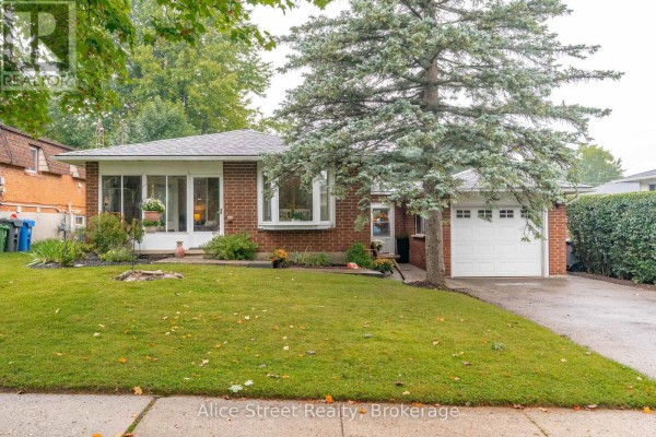 Front exterior of a brick bungalow with green lawn, mature trees, and a white garage. - 5 Glenbrook Drive, Guelph