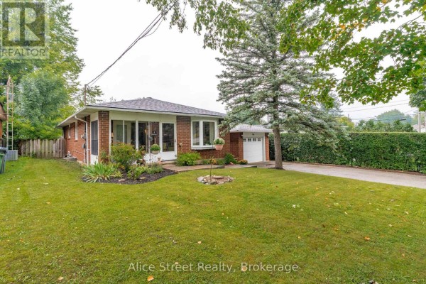 Side view of the red brick bungalow with a manicured lawn, trees, and a white garage. - 5 Glenbrook Drive, Guelph