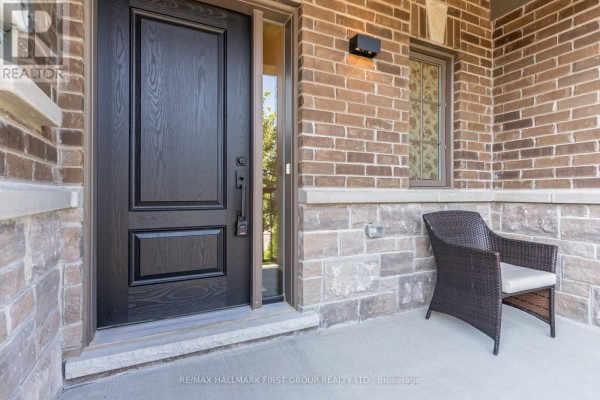 Close-up of dark wood front door and porch with wicker chair, brick and stone exterior. - 5 Harry Thornton Lane, Uxbridge
