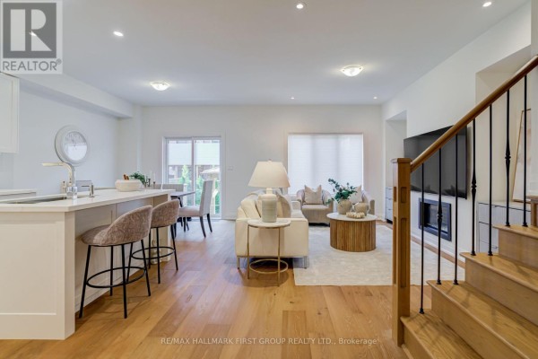 Open-concept living and dining area with kitchen island, bar stools, fireplace, and hardwood floors. - 5 Harry Thornton Lane, Uxbridge