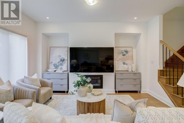 Living room with fireplace, television mounted above, sectional sofas, coffee table, and neutral decor. - 5 Harry Thornton Lane, Uxbridge