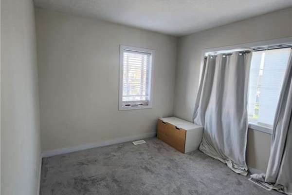 Bedroom with beige walls, grey carpet, a white storage bench, and two windows with curtains. - 5 Keelson Street, Welland