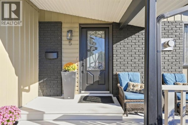 Close-up of the front entrance with a glass-paned door, grey brick, and two blue wicker chairs on the porch. - 5 Lake Huron Bay Se, Calgary