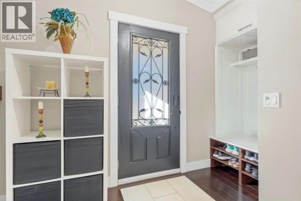 Interior front entrance with a dark grey door, white storage shelves, and a built-in bench with shoe storage. - 5 Lake Huron Bay Se, Calgary