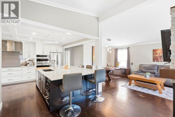 Open-concept kitchen and living area with a large island, white cabinets, stainless steel appliances, and a sectional sofa. - 5 Lake Huron Bay Se, Calgary