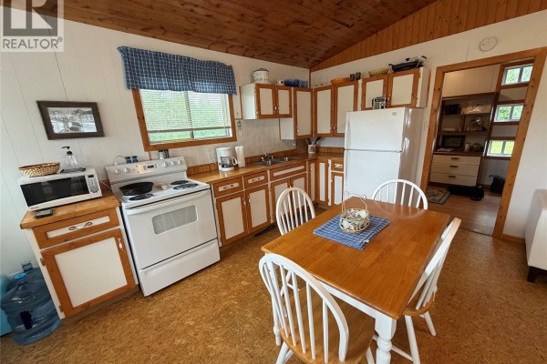 Kitchen with white appliances, wooden cabinets, a stove, microwave, refrigerator, and a small dining table. - 5 Lakeshore Drive, Hudson Bay Rm No  394