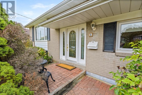 Close-up of the front entrance with a double glass door, brick walkway, and a small metal table. - 5 Lucinda Place, Halton Hills