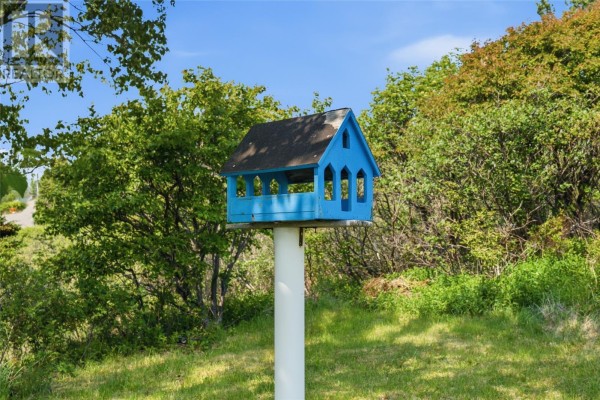 A blue wooden birdhouse with Gothic-style windows sits on a white pole outdoors. - 5 Main Street, Little Bay