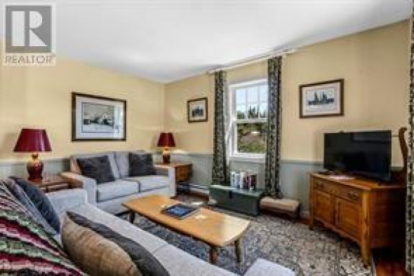 Living room with grey couches, coffee table, and television on a wooden stand. - 5 Marshall’s Hill, Trinity East