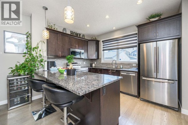 Kitchen with dark brown cabinets, granite countertops, stainless steel appliances, and a central island with seating. - 5 Masters Street Se, Calgary