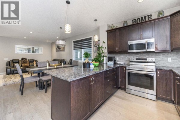 Kitchen and living area with dark brown cabinets, granite island, dining table, seating, and a patterned rug. - 5 Masters Street Se, Calgary