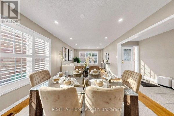 Dining room with a glass-top table set for six and a view into the living room and front entrance. - 5 Mendoza Drive, Brampton