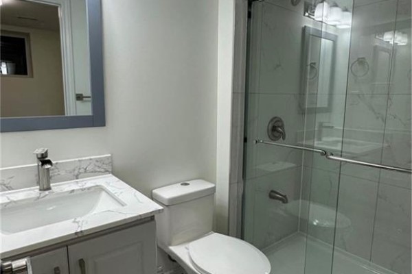 A bathroom with a white vanity, marble-look countertop, toilet, and a glass-enclosed shower. - 5 Munro Circle Unit# Lower, Brantford