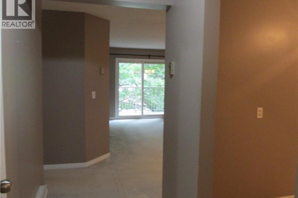 View from entrance hallway into a carpeted living area with large sliding glass doors. - 5 Niagara Street Unit# 203, Grimsby