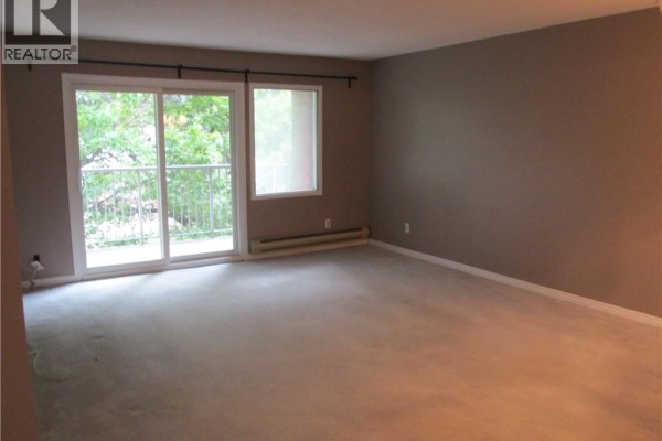 Living room with beige carpet, gray walls, a sliding glass door, and a square window. - 5 Niagara Street Unit# 203, Grimsby