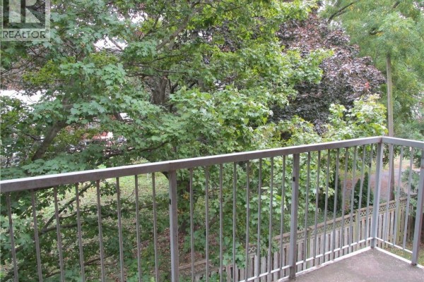 Balcony with metal railing overlooking lush green trees and surrounding foliage. - 5 Niagara Street Unit# 203, Grimsby