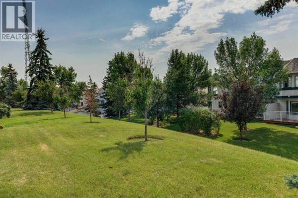 Grassy common area with scattered trees and townhouses in the background. - 5 Prominence View Sw, Calgary