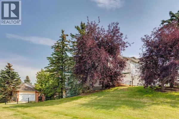 Side view of townhouses with mature trees and a sloped lawn. - 5 Prominence View Sw, Calgary