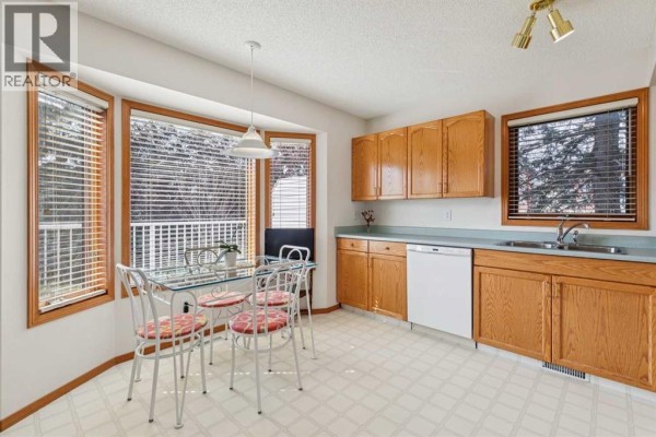 Kitchen and dining area with light wood cabinets, white appliances, and a glass-top table. - 5 Prominence View Sw, Calgary
