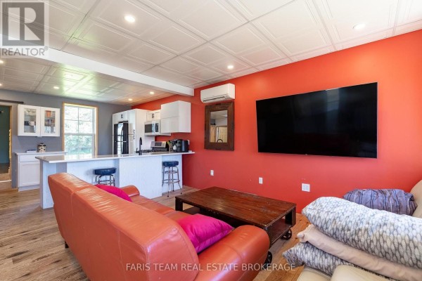 Living room with orange walls, a sectional sofa, coffee table, and a large television. - 5 Scott Street, Penetanguishene