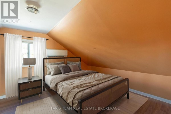 Bedroom with an orange sloped ceiling, a bed, nightstand, and a window with white curtains. - 5 Scott Street, Penetanguishene