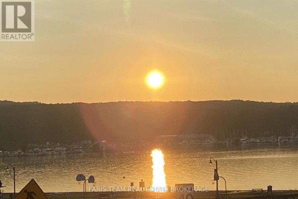 Sunset over a bay with boats docked and a tree-lined horizon, reflecting on the water. - 5 Scott Street, Penetanguishene