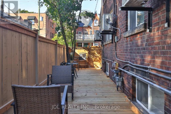 Wooden deck with chairs and a brown wooden fence along the side of a brick building. - 5 Sorauren Avenue, Toronto