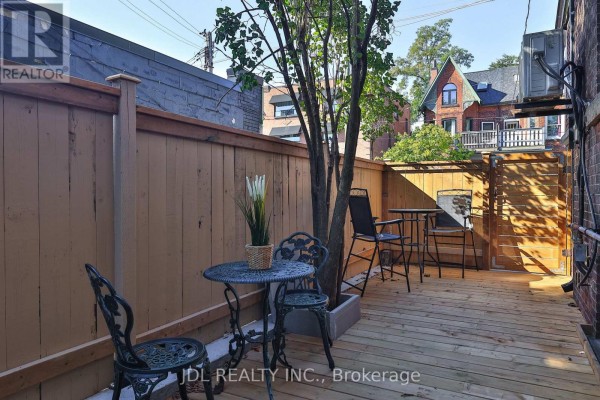 Outdoor patio area with dark metal table and chairs on a wooden deck. - 5 Sorauren Avenue, Toronto