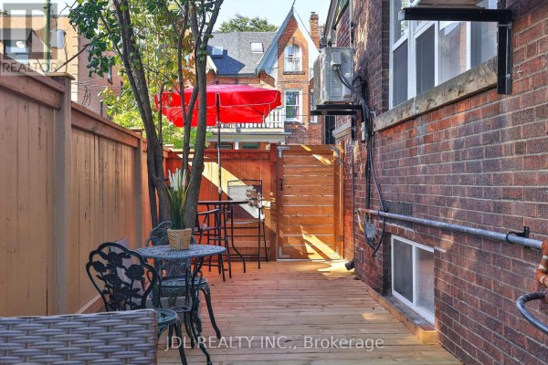 View of a wooden deck and fence with a red umbrella and outdoor seating. - 5 Sorauren Avenue, Toronto