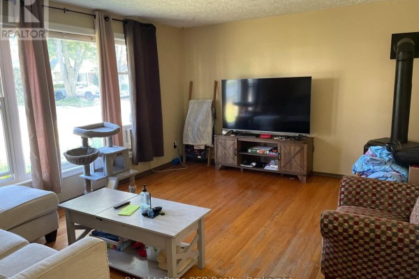 Living room with hardwood floors, a sofa, coffee table, entertainment center, and a wood stove. - 5 Stinson Street, South Bruce