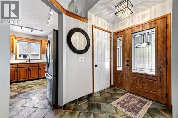 Interior entryway with slate tile flooring, wood double doors, and a glimpse of the kitchen. - 5 Sunset Crescent, Okotoks