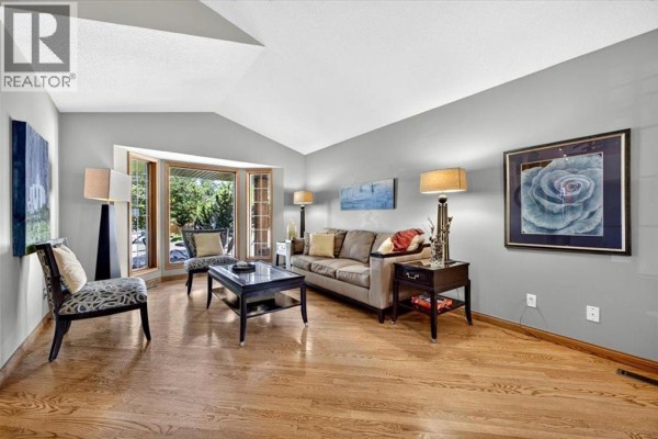 Living room with hardwood floors, a sofa, two chairs, a coffee table, and a bay window. - 5 Sunset Crescent, Okotoks
