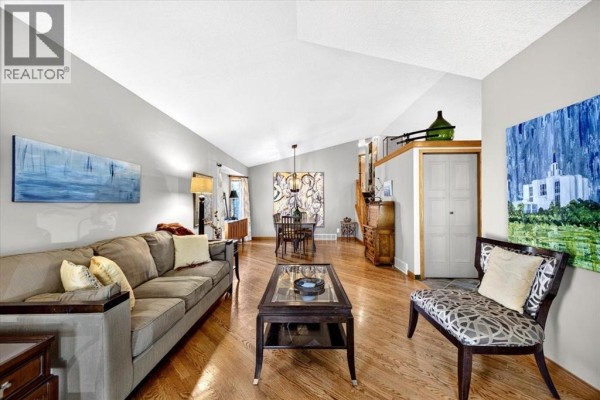 Living room with hardwood floors, sofa, two chairs, coffee table, and large artwork on wall. - 5 Sunset Crescent, Okotoks