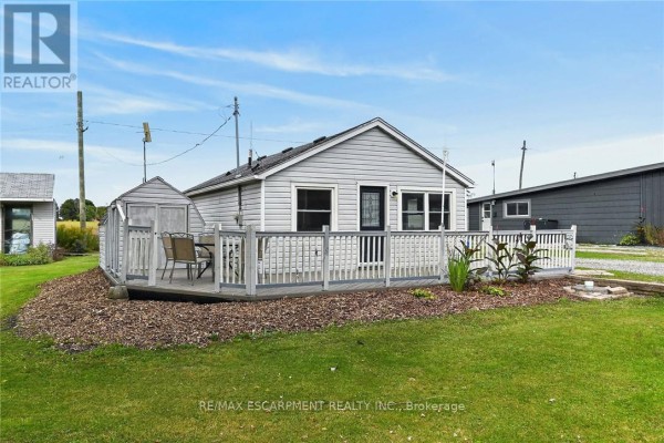 Rear exterior of a grey vinyl-sided bungalow with a wooden deck and seating area. - 5 Willoway Lane, Haldimand