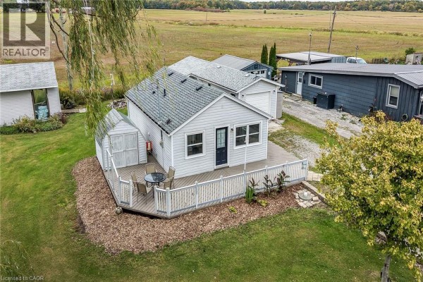 Aerial view of the bungalow, deck, and garage with a backdrop of green fields and trees. - 5 Willoway Lane, Selkirk