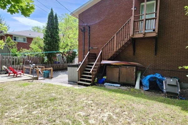 Backyard with a wooden staircase, storage bins, and red chairs on a patio. - 50 Albany Street, Sudbury